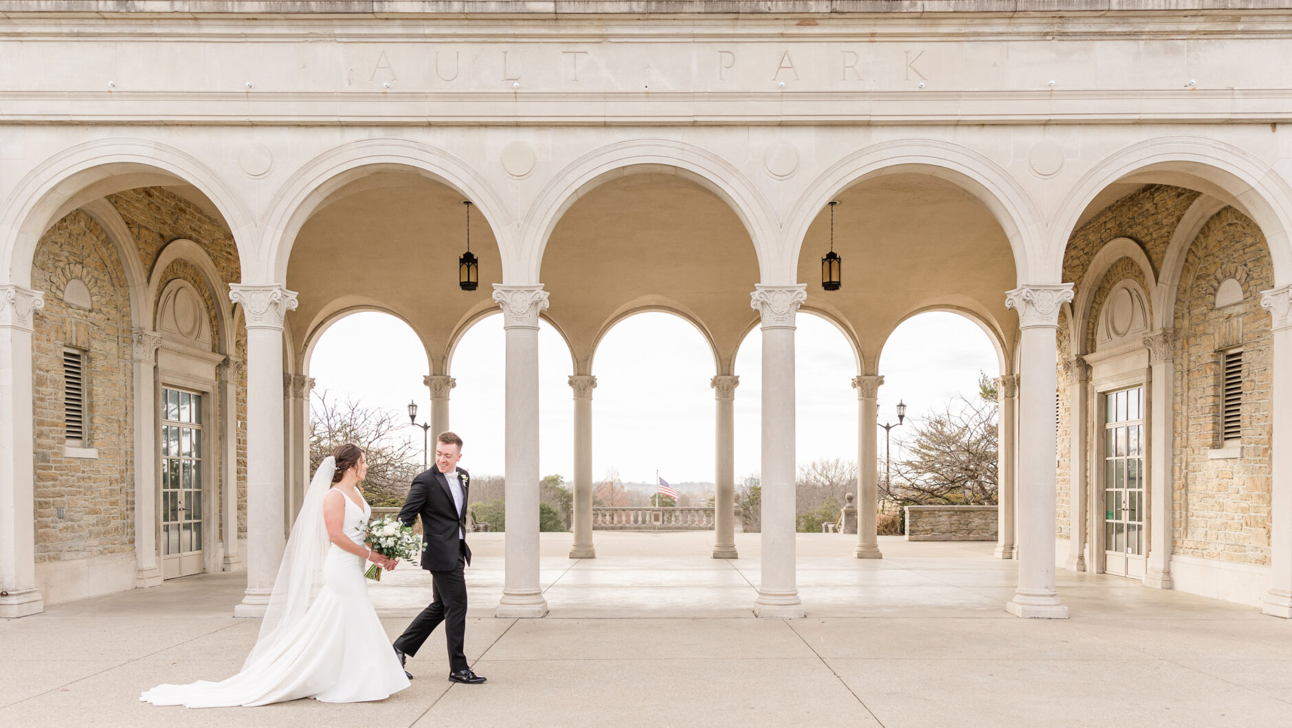 Bride and Groom holding hands in front of stone carved archways at Ault park at sunset