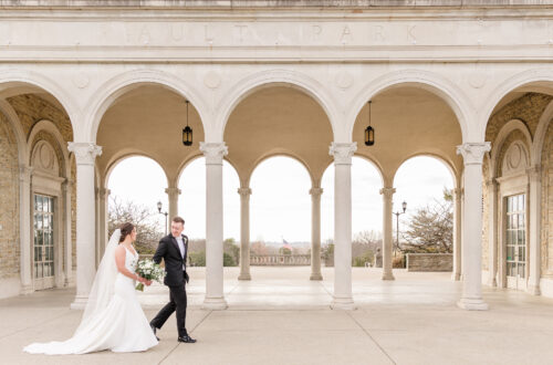 Bride and Groom holding hands in front of stone carved archways at Ault park at sunset
