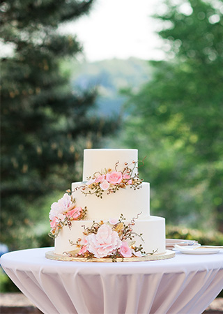 A white wedding three tier wedding cake decorated with pink flowers on a table at Alms Park