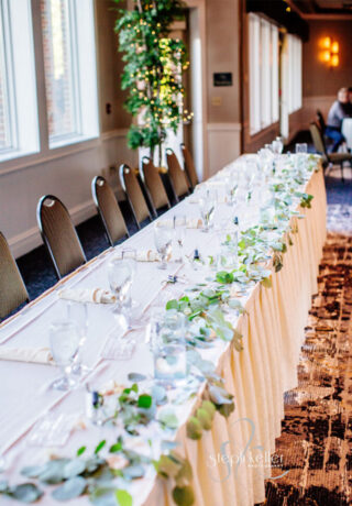 long wedding table with white table cloth, glasses, and flowers