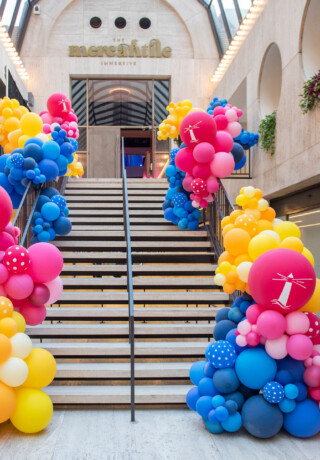 A staircase decorated with colorful balloon clusters in a modern indoor space.