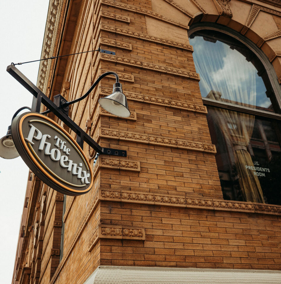 A sign reading “The Phoenix” hangs outside a brick building with a large arched window.