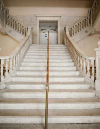 Wide marble staircase with ornate railings splits into two directions; columns and archways on both sides.